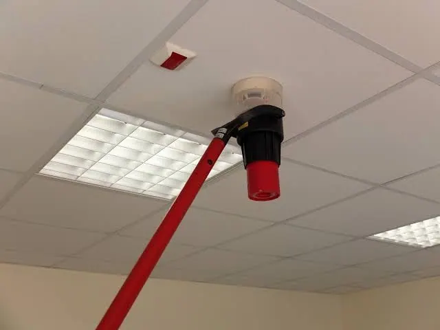 Photo-electric smoke detector removed for inspection, its label showing a 1993 manufacture date, assessed for end of life by Safe QLD Fire Protection