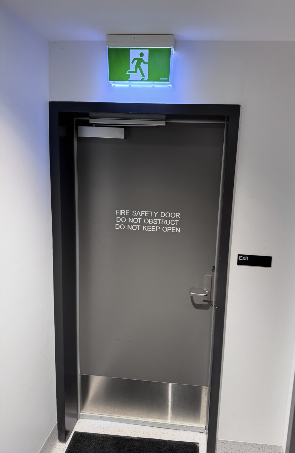 Grey fire safety door with DO NOT OBSTRUCT signage and exit sign, inspected by Safe QLD Fire Protection