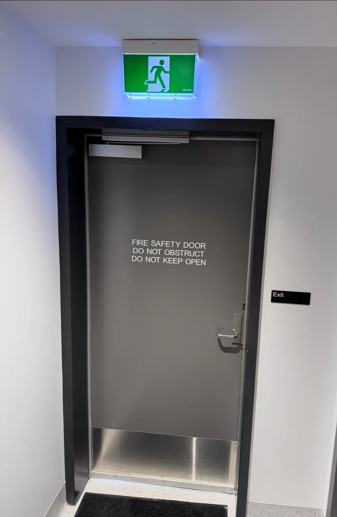 Grey fire safety door with do not obstruct signage and exit sign in a commercial building